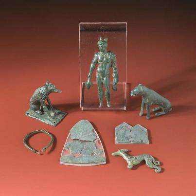 Photo: A group of objects from Llys Awel, near Pen-y-Corddyn hillfort. Altogether 535 Roman coins were found dating from the late 1st century to the end of the 4th century, two small bronze seated dogs, another dog of greyhound type, a statuette of Mercury, three votive plaques (two decorated with dogs) and a twisted wire bracelet. The role of the dog in both the Celtic and Classical world appears to be concerned mainly with healing. The presence of the dogs in this assemblage would appear to indicate a healing shrine in the vicinity or possibly a curative spring. The coins and objects would have been offered to the gods by those seeking a cure. Such a shrine may have had pre-Roman origins and was certainly patronised until the 390s.